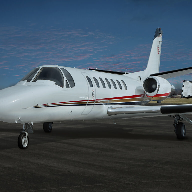 A small white private jet parked on the runway under a clear blue sky.