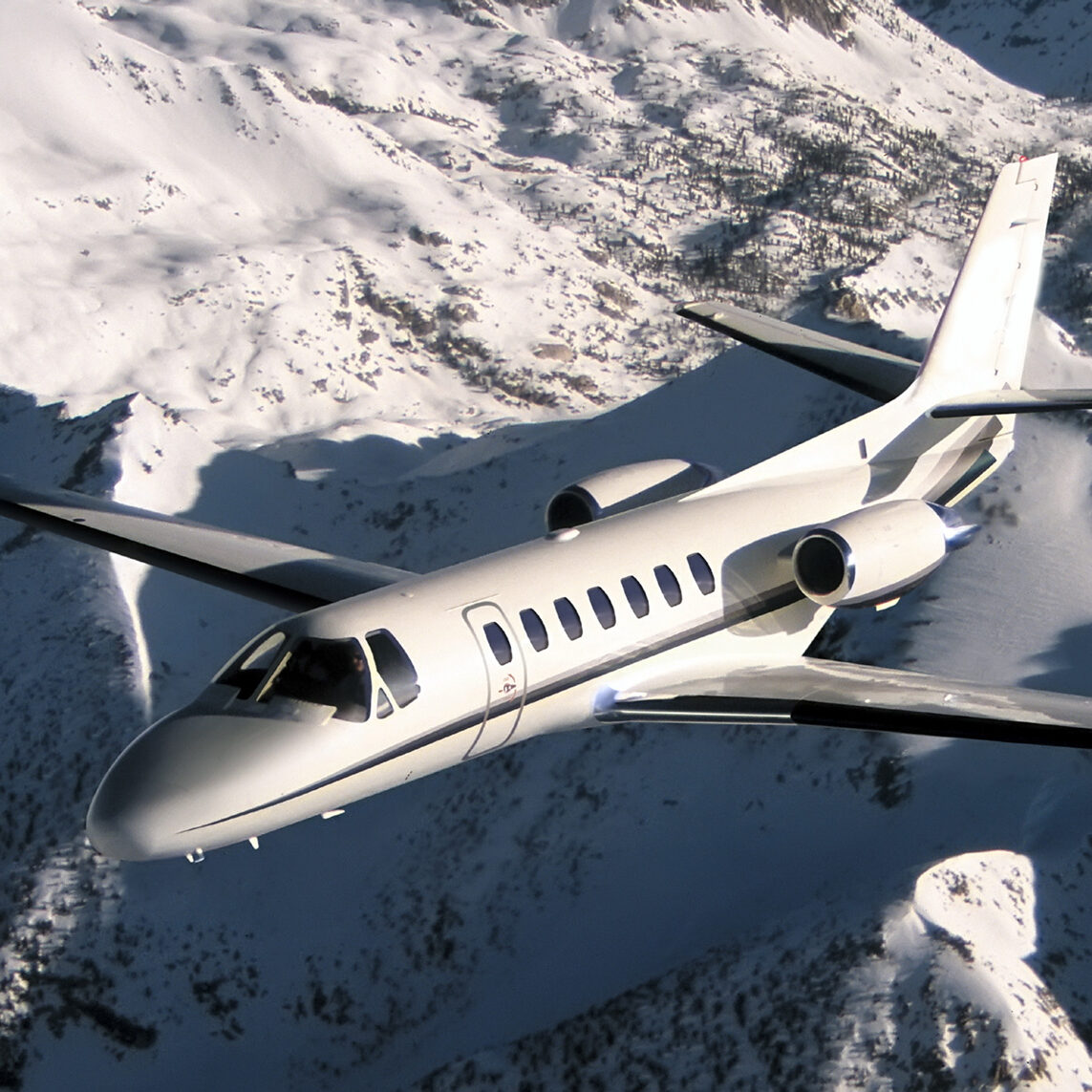 A white private jet flying over snow-covered mountains.