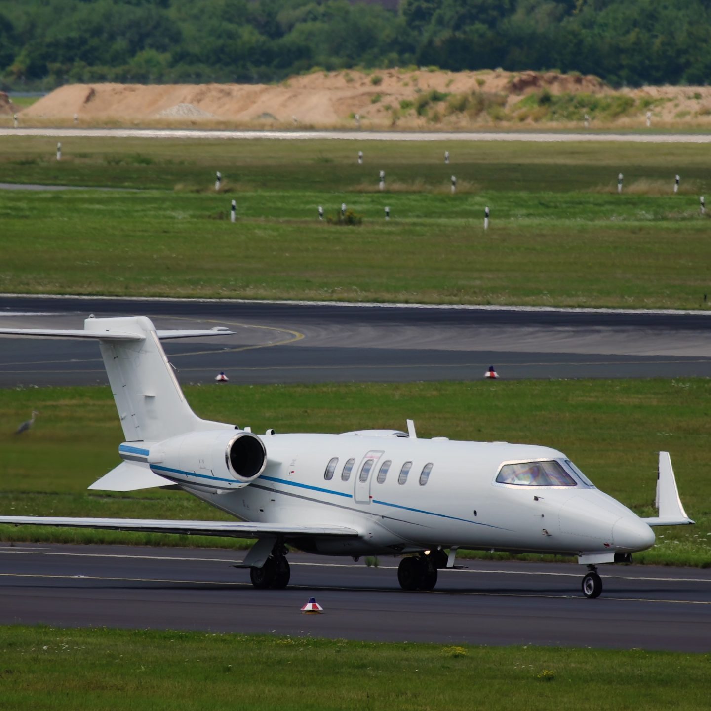 Private jet taxiing on runway at airport with green surroundings.