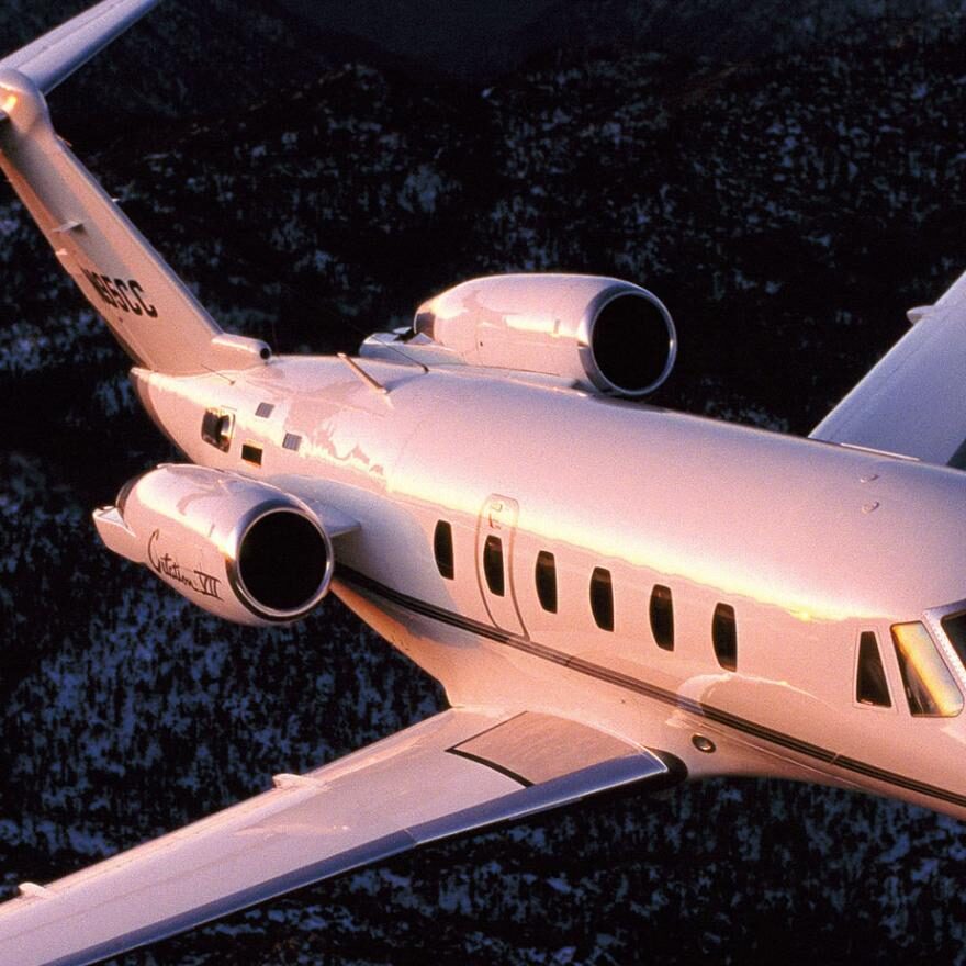 A private jet flying over a mountainous landscape during sunset.