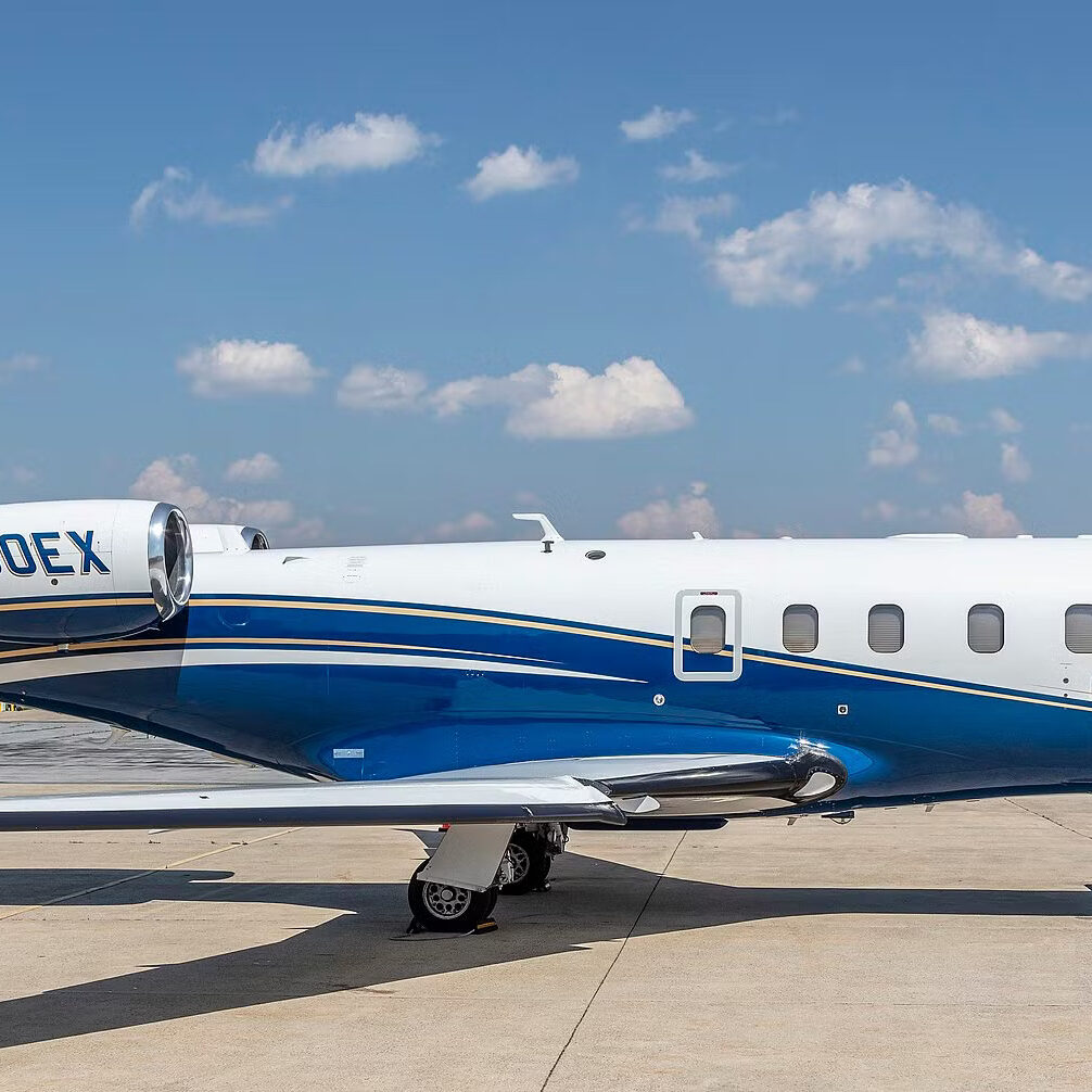 Small private jet parked on the runway under a blue sky.