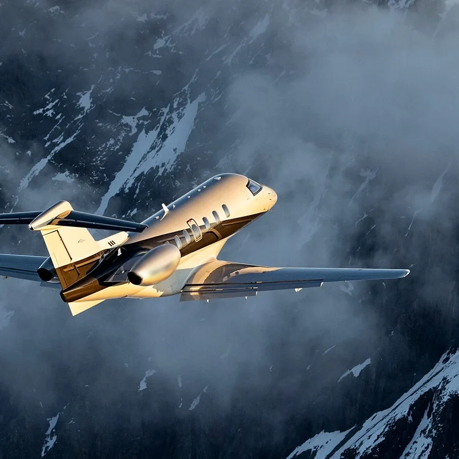 Private jet flying above snowy mountain peaks in cloudy weather.